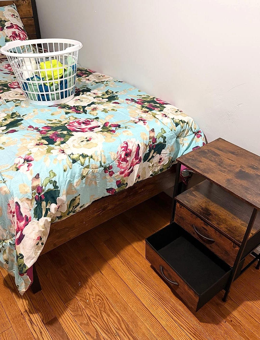 Fully furnished resident bedroom with a made twin bed, clean linens, and a wooden bedside table