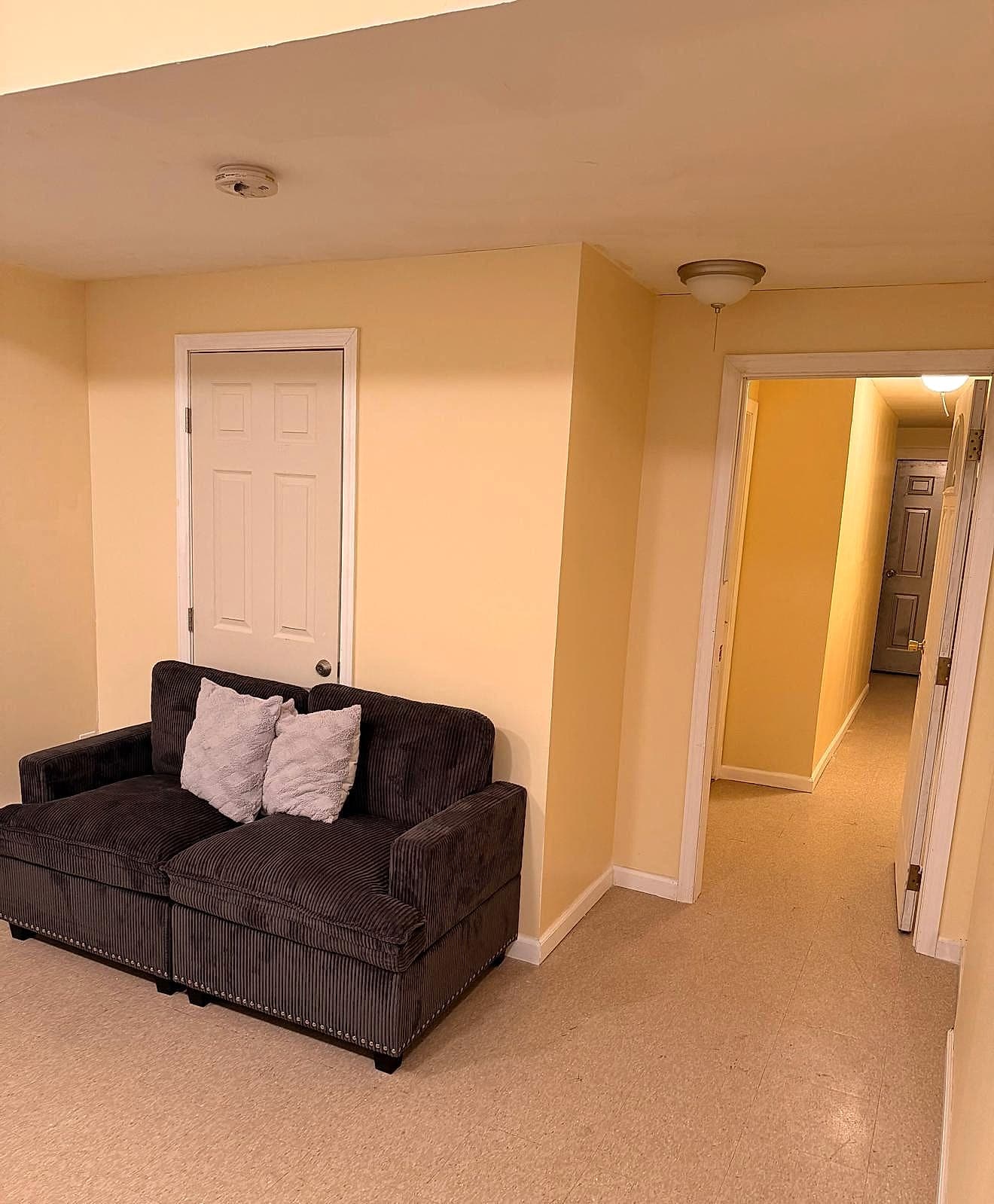 Clean lounge with loveseat and hallway leading to resident rooms in New York City