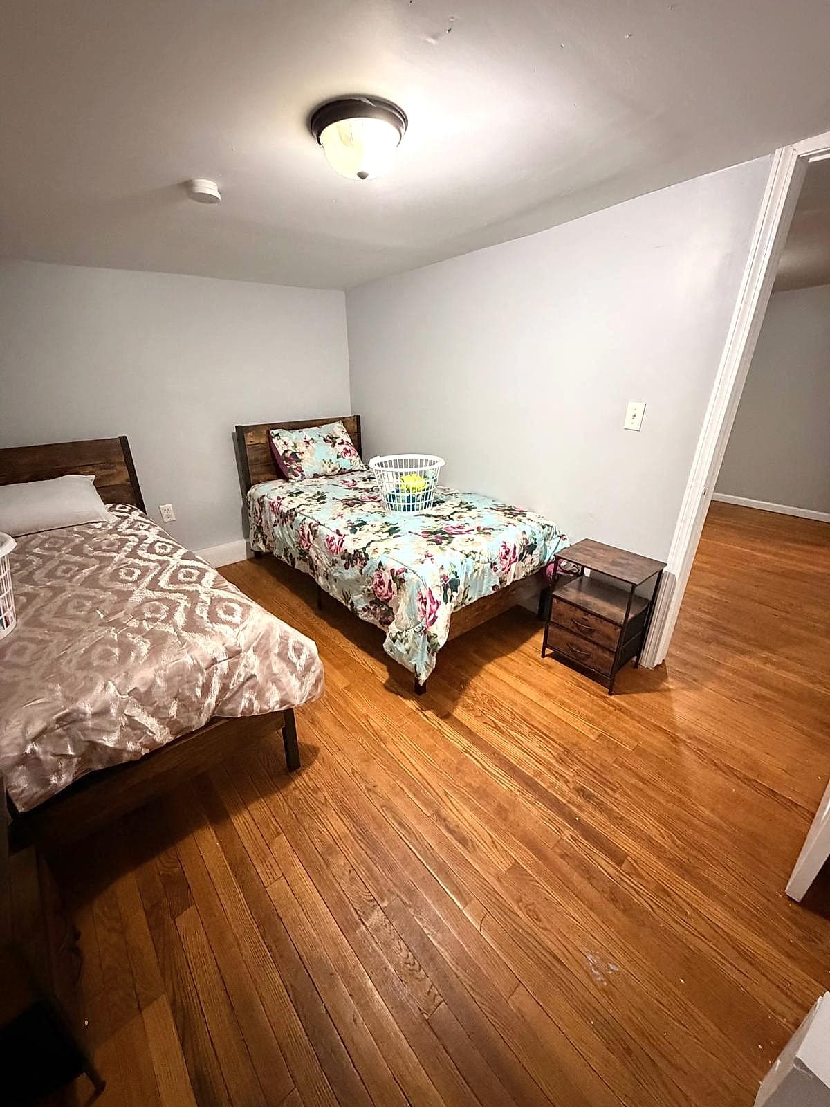 Shared resident bedroom with two twin beds, made linens, hardwood flooring, and bedside table
